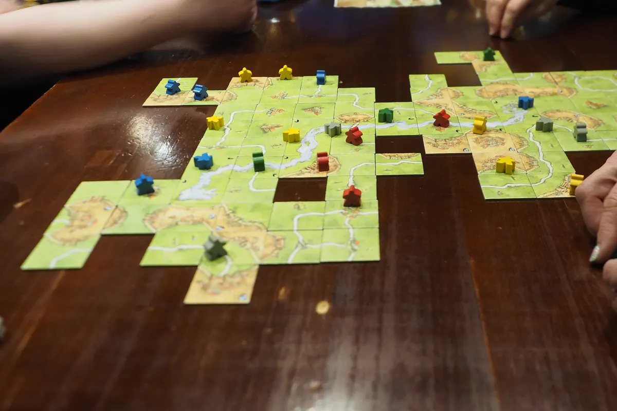 Carcassonne in progress on a wooden pub table: landscape tiles with roads, rivers and cities dotted with colored meeples