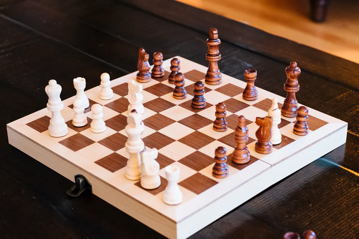 Wooden chess set mid-game on a folding board, light and dark pieces facing off on a dark wooden table