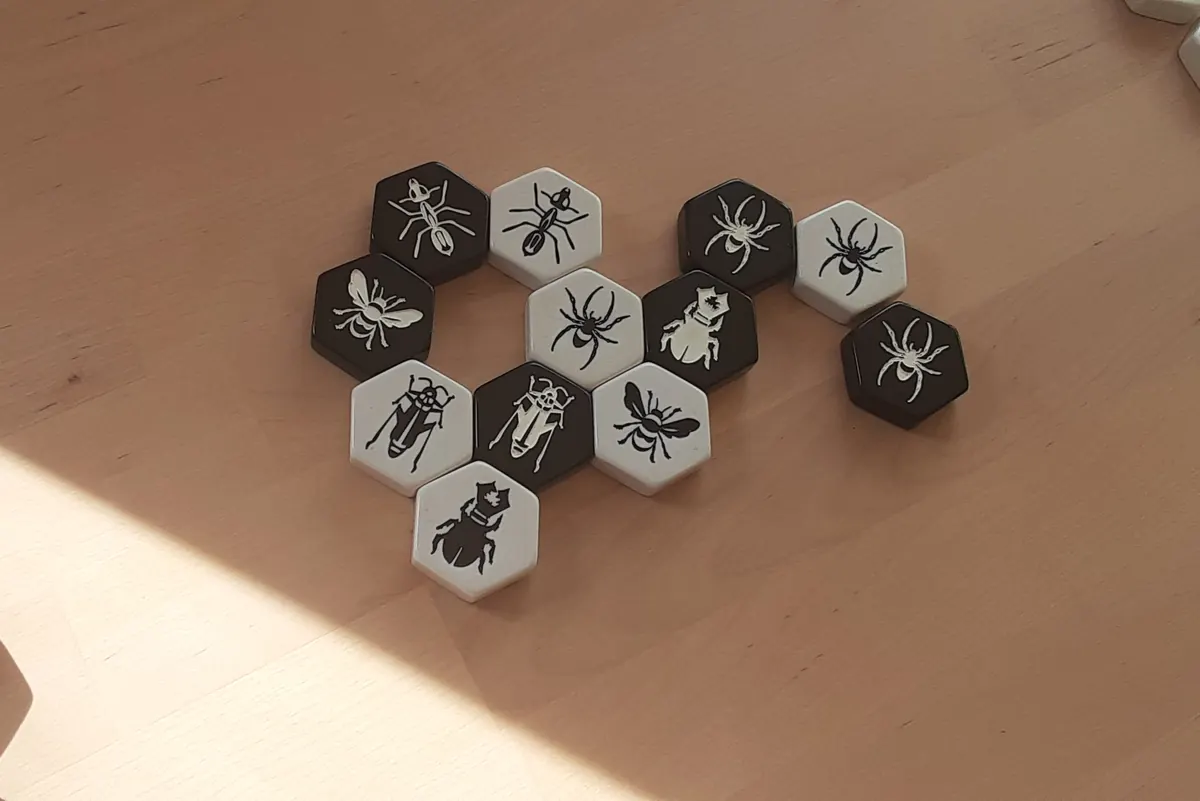 Black and white Hive Carbon Edition tiles with insect symbols forming a hive on a sunlit wooden table