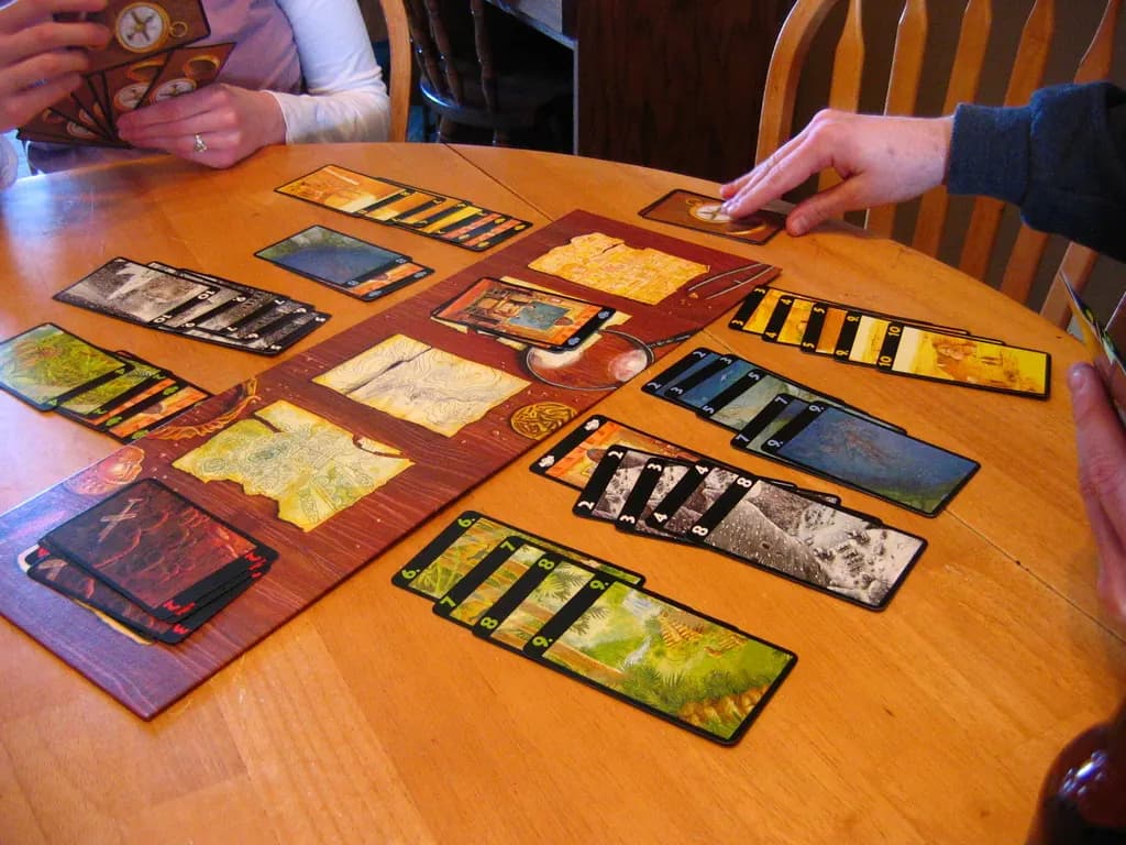 Lost Cities on a wooden table, colored expedition card columns laid out on both sides of the central board
