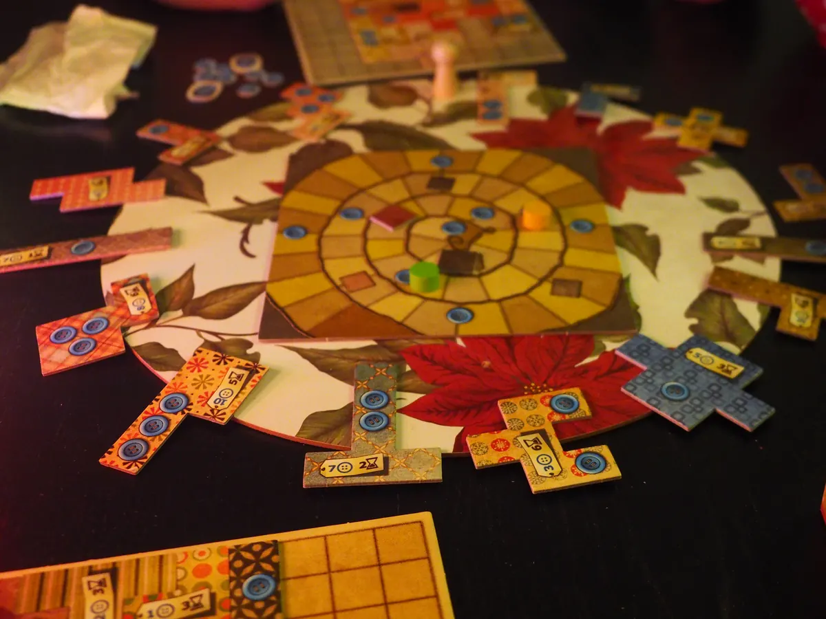 Patchwork near the end of play: spiral time-track board ringed by fabric-patterned patch tiles with blue button icons