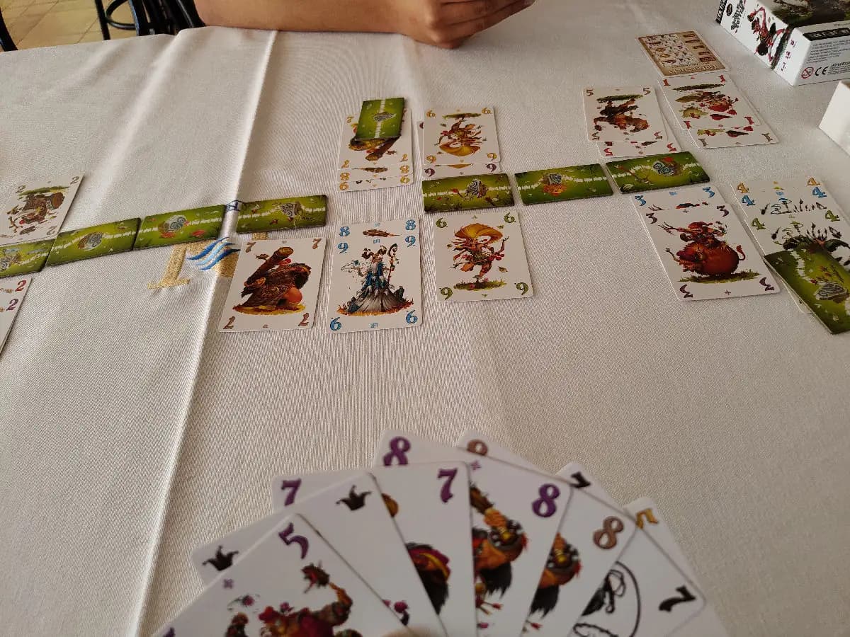 Schotten Totten in play on a white tablecloth: border stones lined up between clan cards, a hand of cards in front