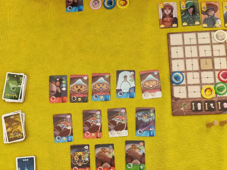 Splendor Duel development cards in a pyramid beside the gem token board and royal cards on a yellow tablecloth