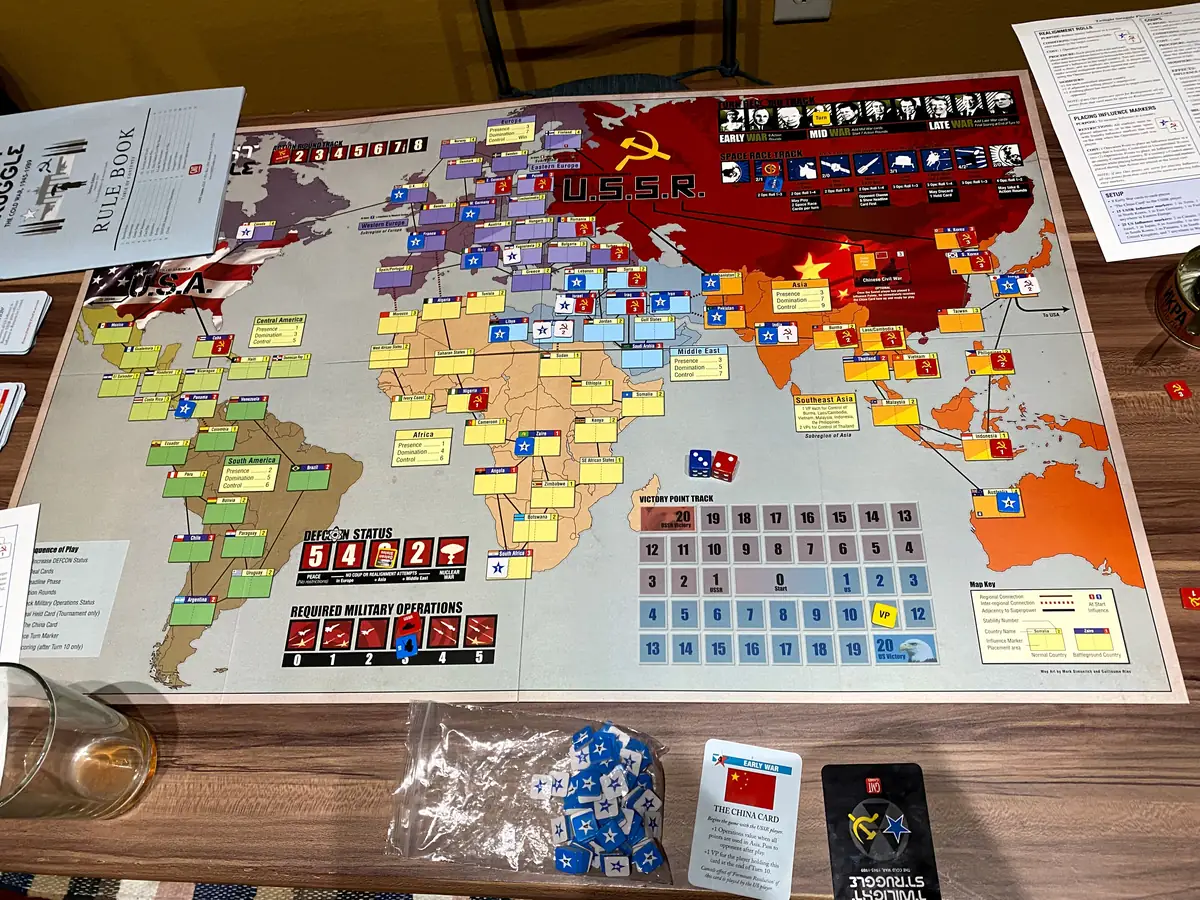 Twilight Struggle mid-war on a wooden table: world map board covered in US and USSR influence markers, dice and cards
