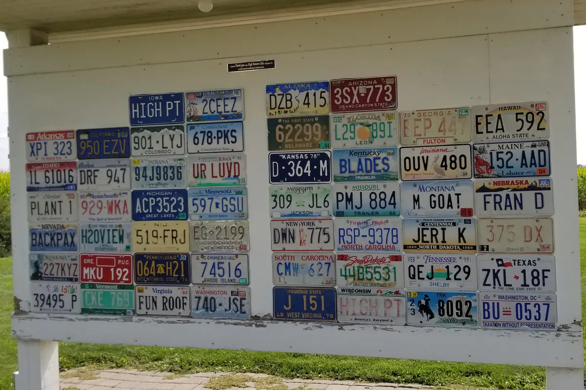 Outdoor display board with dozens of colorful US state license plates, including Iowa, Texas, Hawaii and Montana